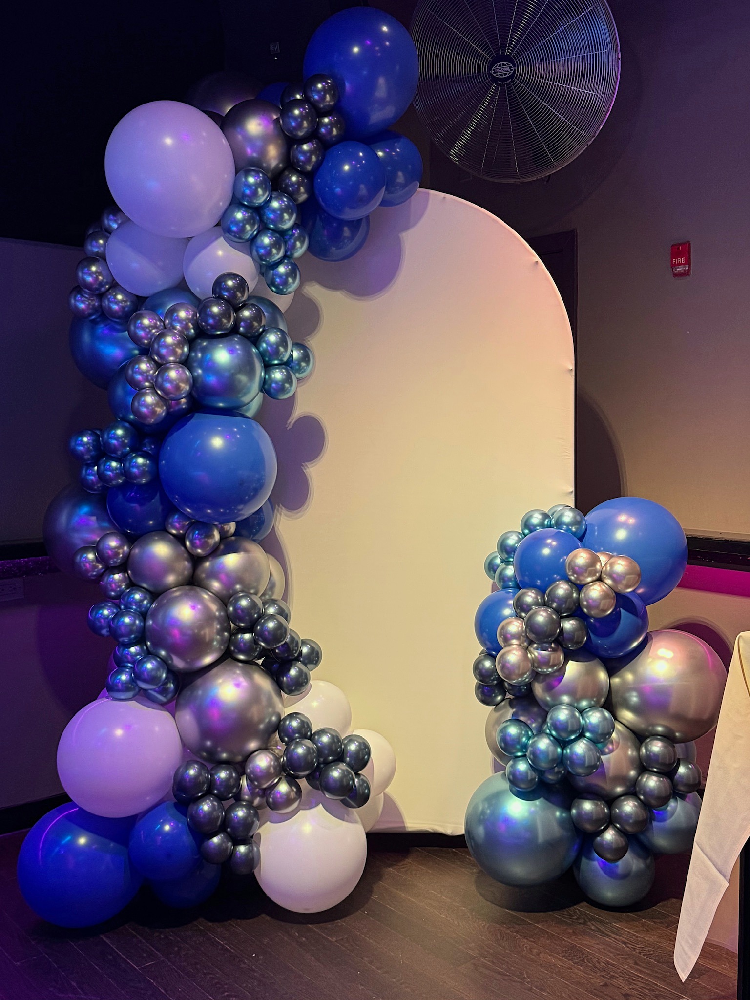 Blue, lavender and iridescent organic balloon installation around a rounded backdrop